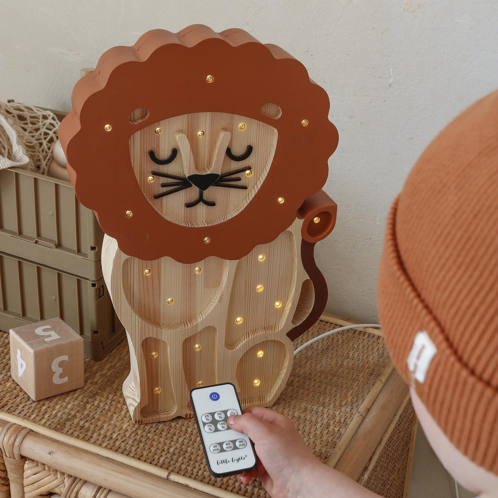 Wooden Little Lights Lion night light with a child holding a remote control on a wicker dresser in a kid's room