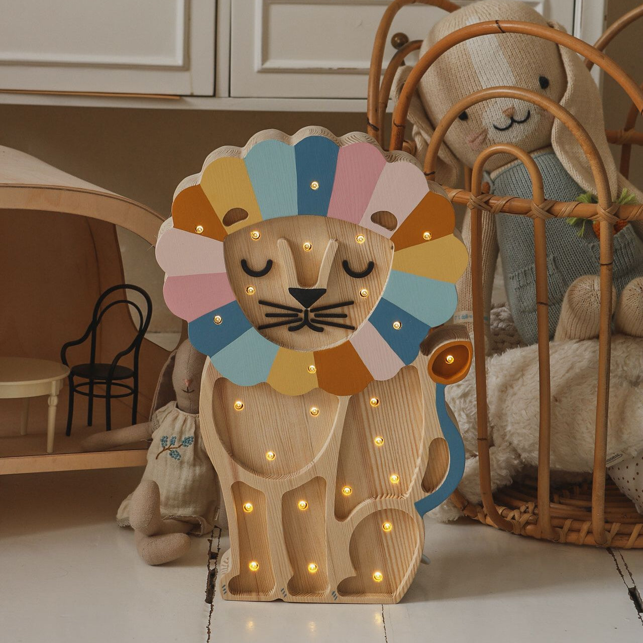 Little Lights Wooden Lion night light in a kid's room next to a basket with toys