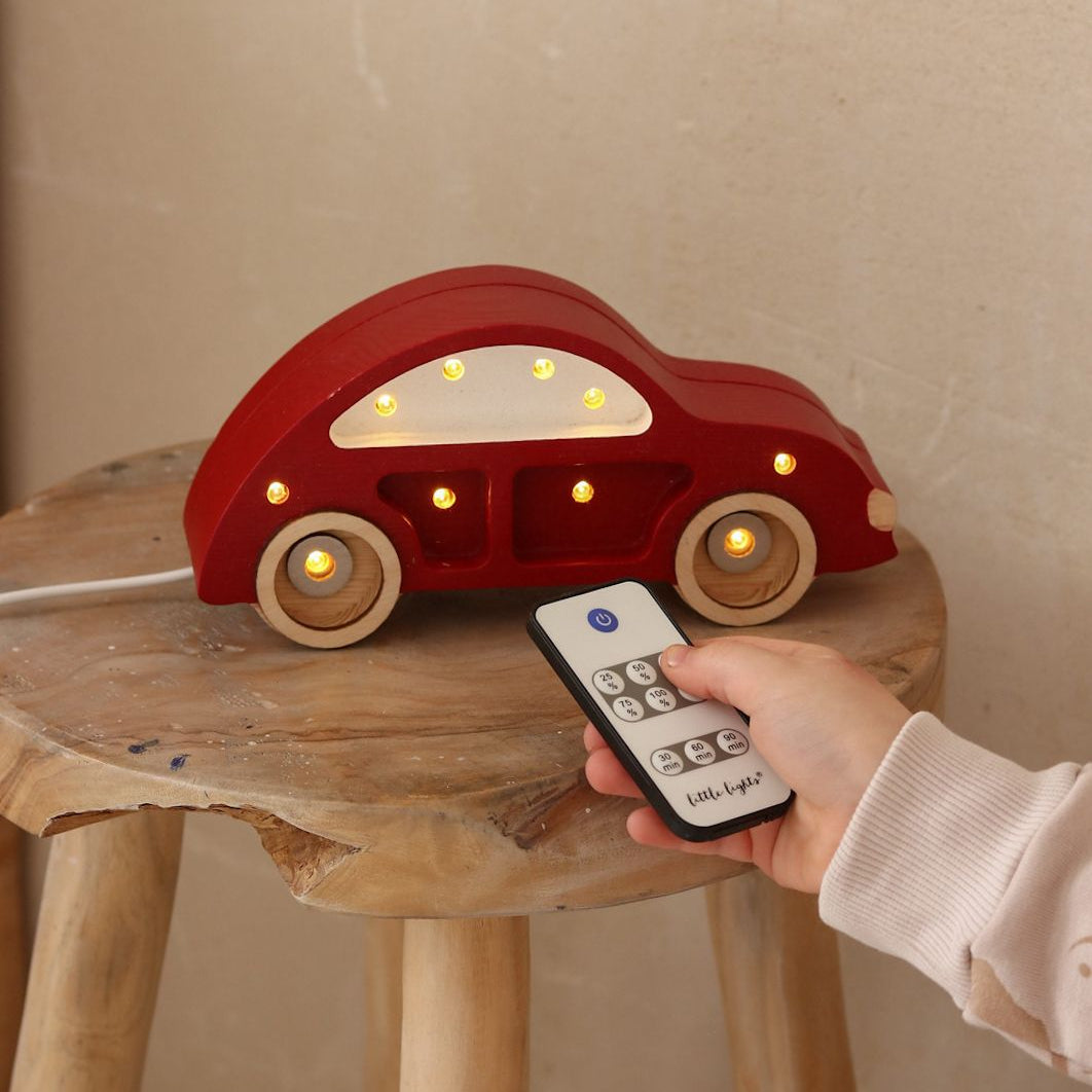 A boy dimming the Little Light red Mini Beetle Car Night Light with the remote