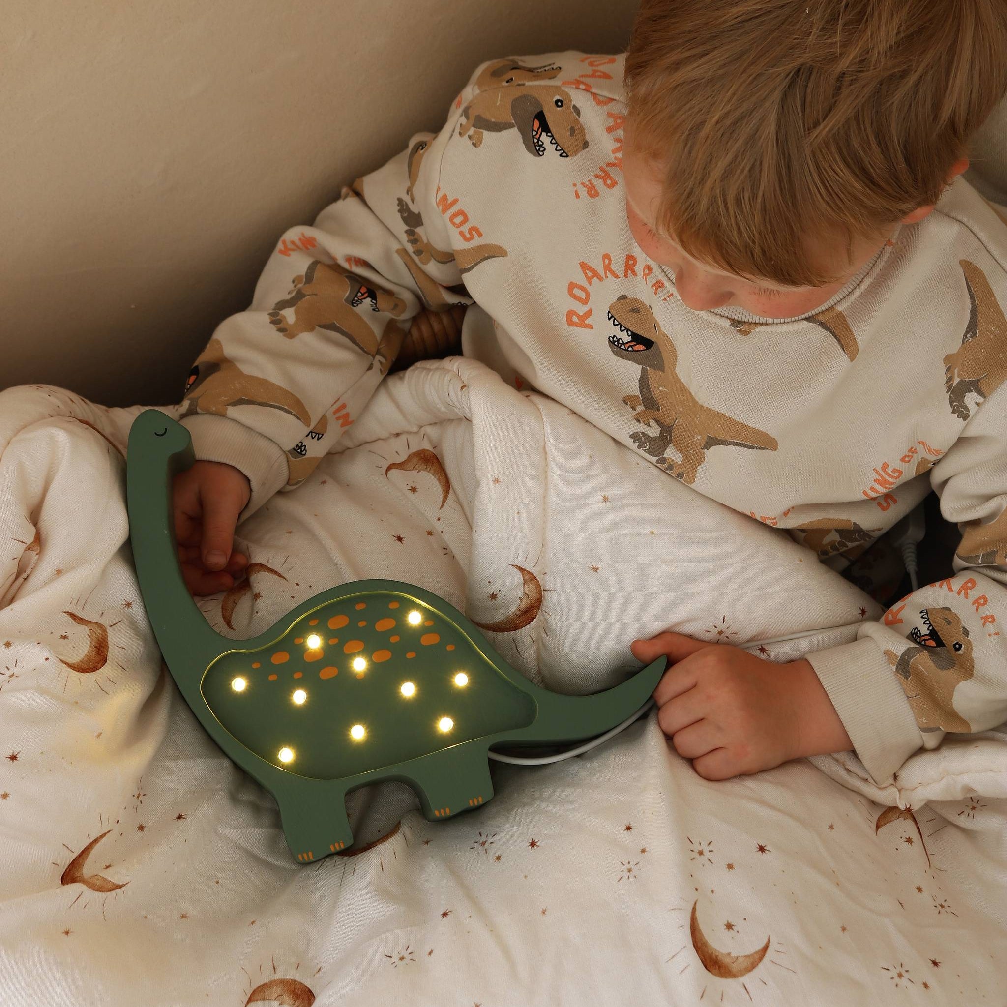 Boy in dinosaur-themed pajamas holding a green dinosaur night light.