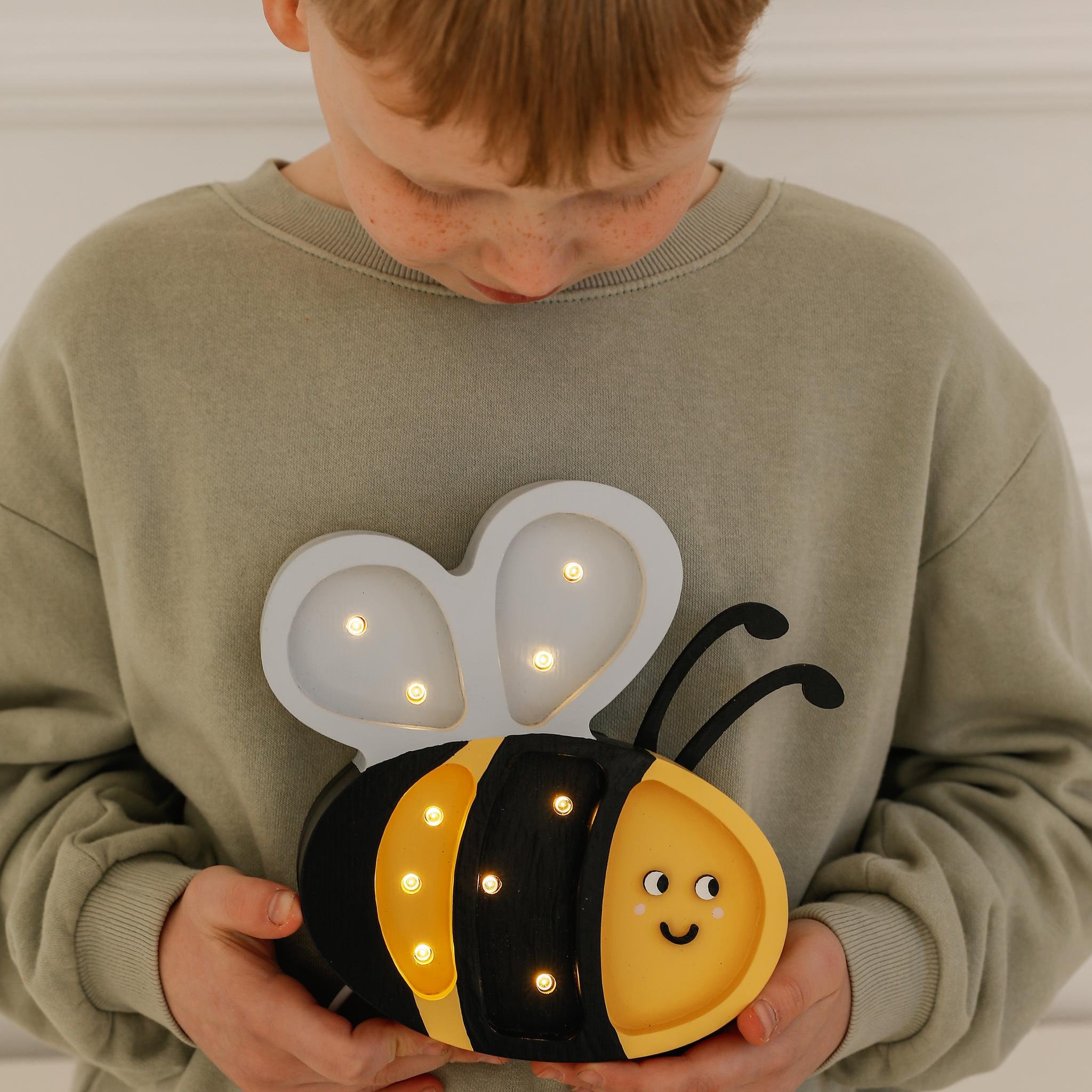 A boy holding Little Lights Mini Happy Bee lamp
