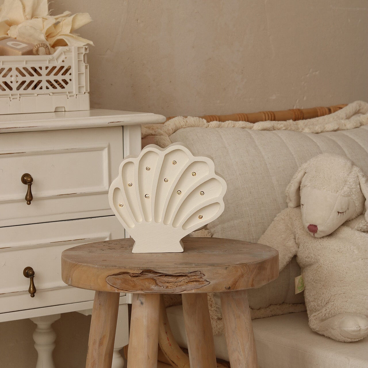 Decorative white shell night light on a wooden stool with a white dresser and plush toy in the background