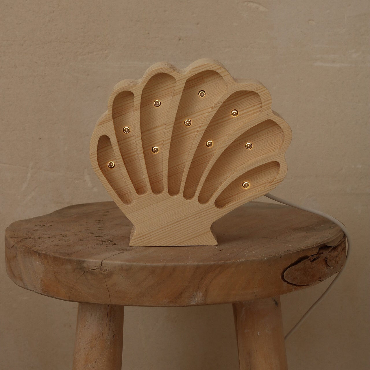A natural wood shell-shaped night light with small gold LED bulbs inside, displayed on a rustic wooden stool against a textured beige wall.