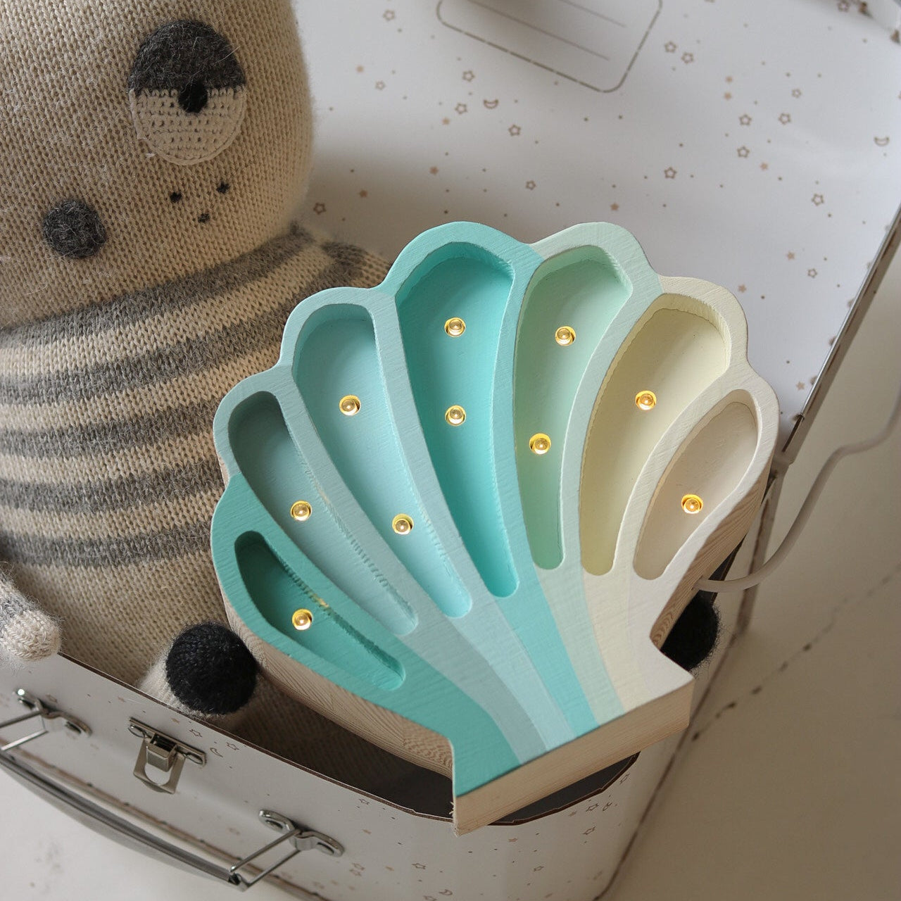 Light blue Shell night light by Little Lights inside an open suitcase with a plush toy next to it.