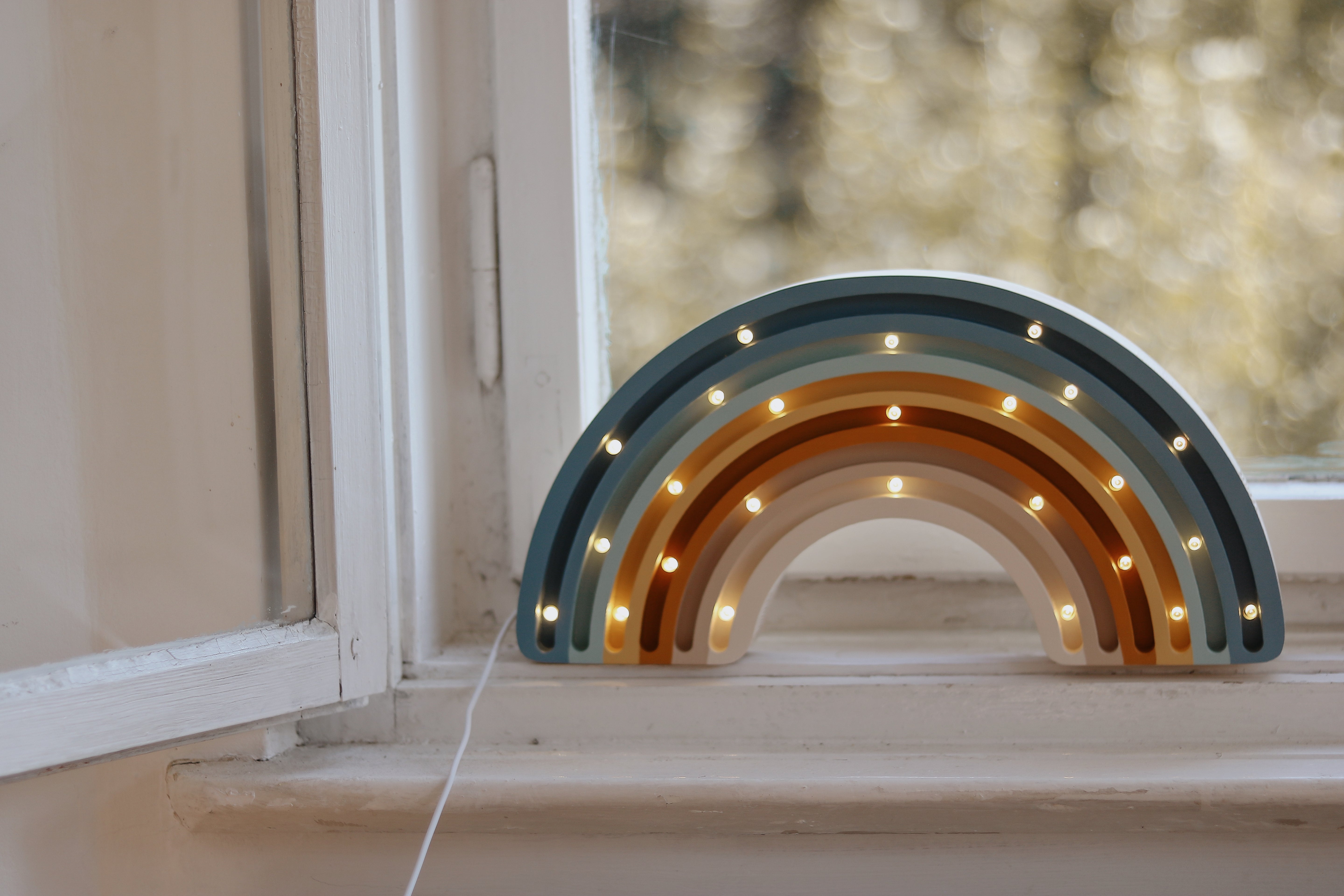 Decorative rainbow-shaped light on a windowsill with an outdoor background