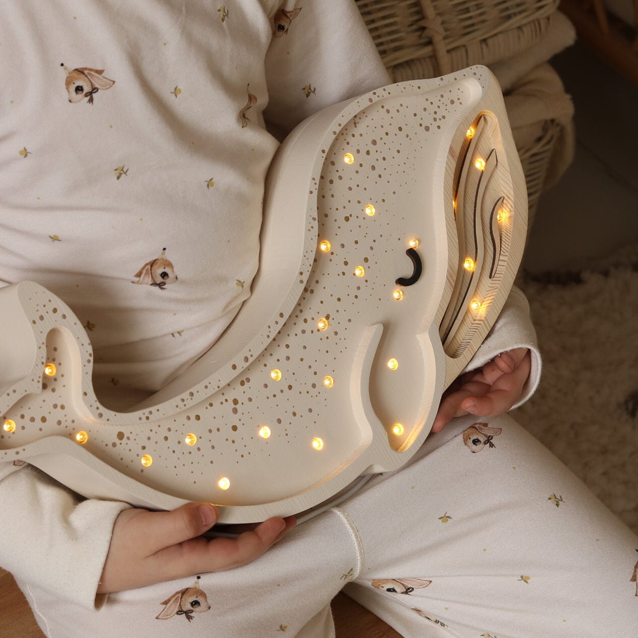Child holding white Little Lights Whale night light in a cozy indoor setting
