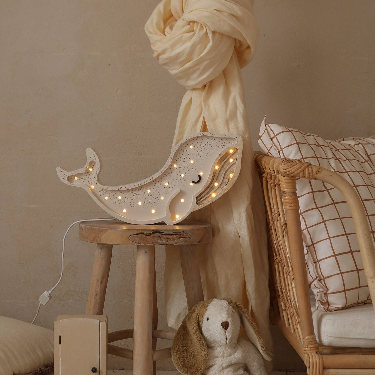 Little Lights White Whale night light on a stool by the bed in a cozy baby room