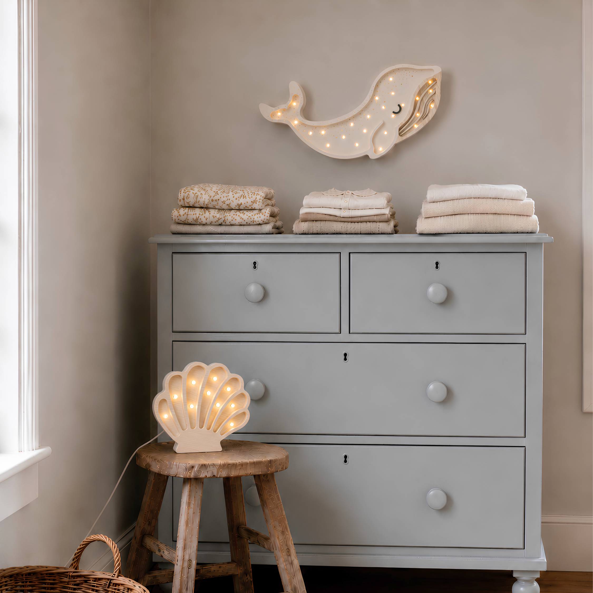 White Whale Night Light hanging above the dresser in a abby nursery with white Seashell Lamp glowing softly on a wooden stool